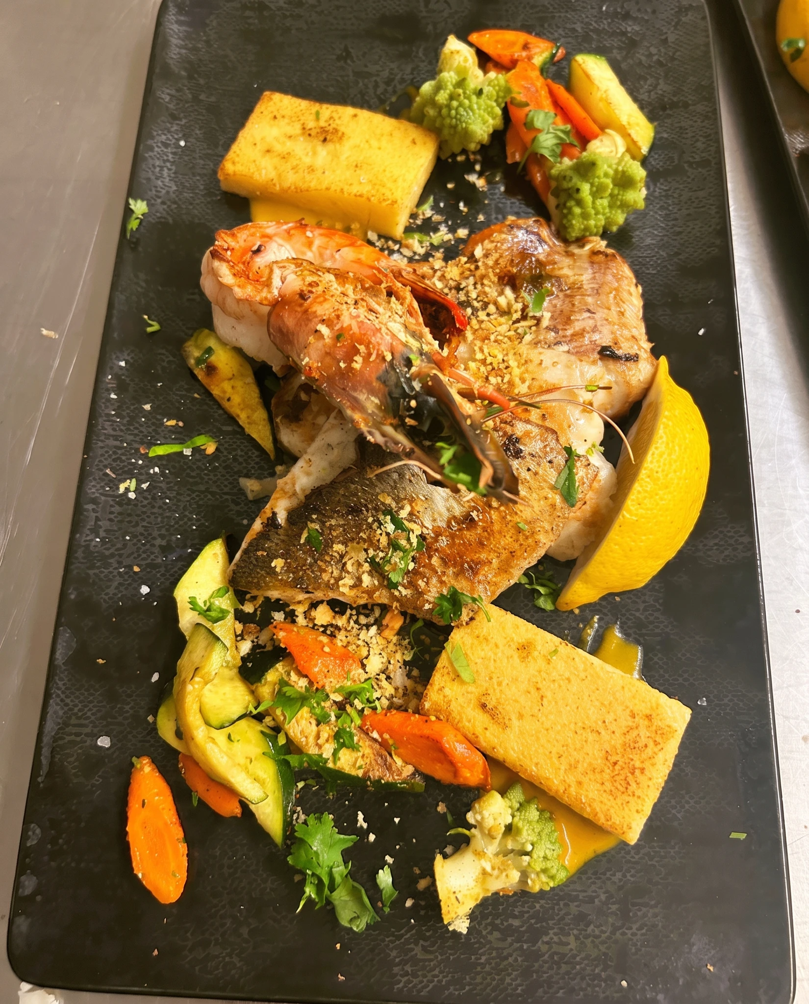Filet de bar et poisson blanc en croûte dorée, gambas grillée, polenta grillée et légumes confits